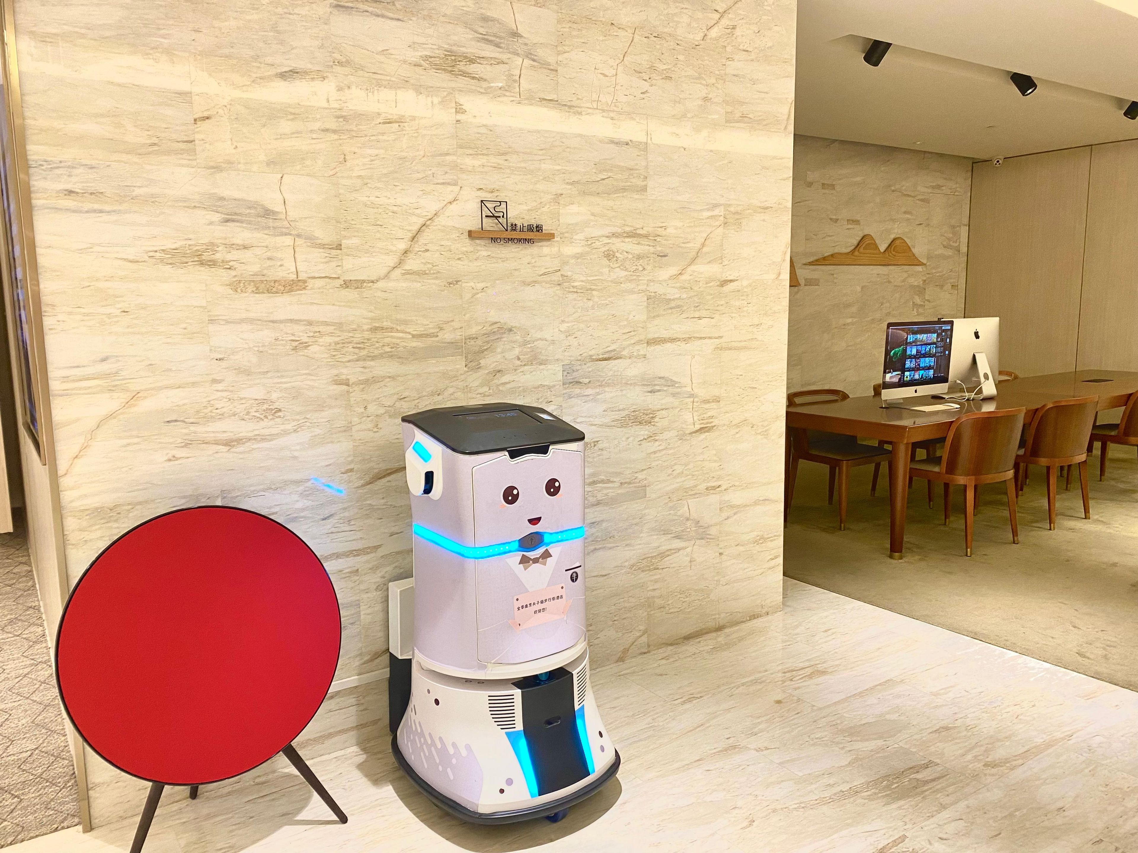 Ein Roboter in einem modernen Raum mit einer Marmorwand, einem roten Tisch und einem Holzesstisch mit Stühlen.