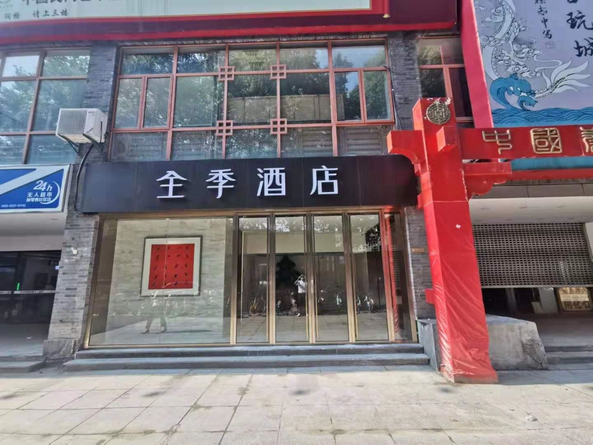 L’entrée d’un hôtel, avec une porte en verre, un auvent rouge et une enseigne en caractères chinois.