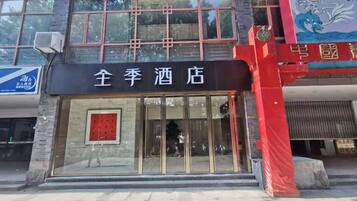 L’entrée d’un hôtel, avec une porte en verre, un auvent rouge et une enseigne en caractères chinois.