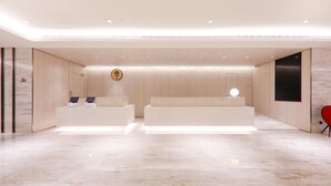 A modern reception area with a marble floor, two reception desks, a wall-mounted clock, and a red chair. - Ji Hotel (nanjing Confucius Temple Pedestrian Stre (Nanjing)