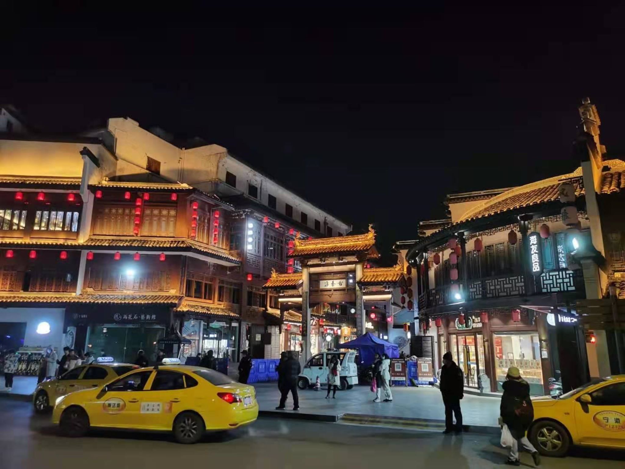 A traditional building with multiple stories, illuminated by warm lighting, and a street with yellow taxis.