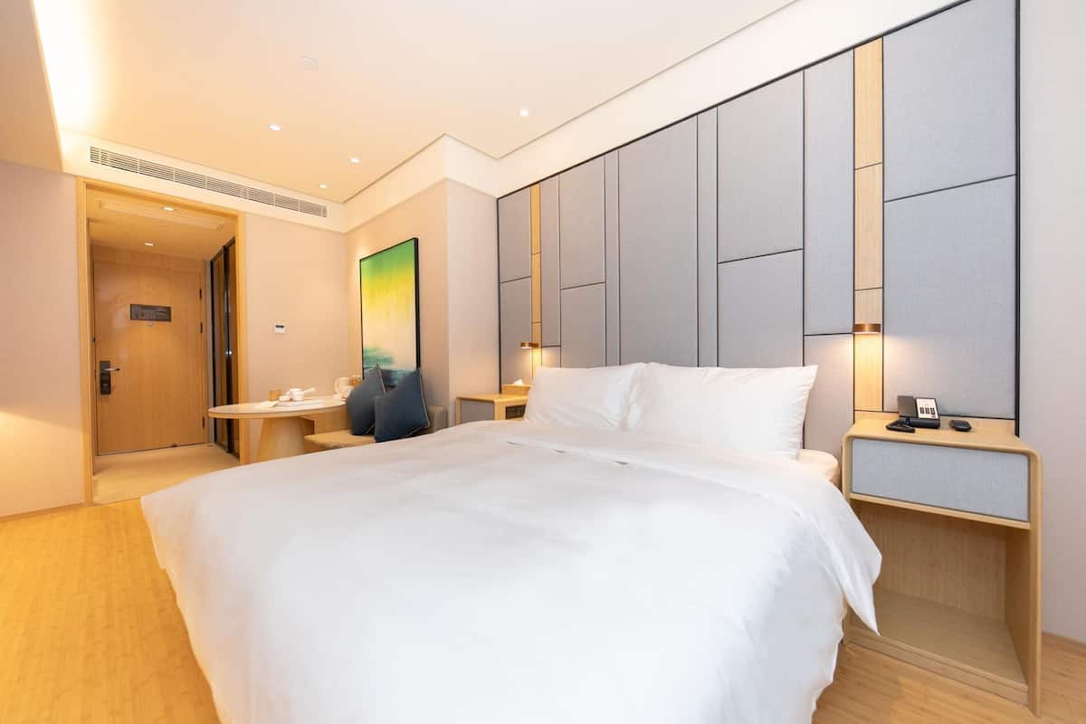 Una habitación de hotel con una cama grande, mesitas de noche, un escritorio y un cuadro en la pared.