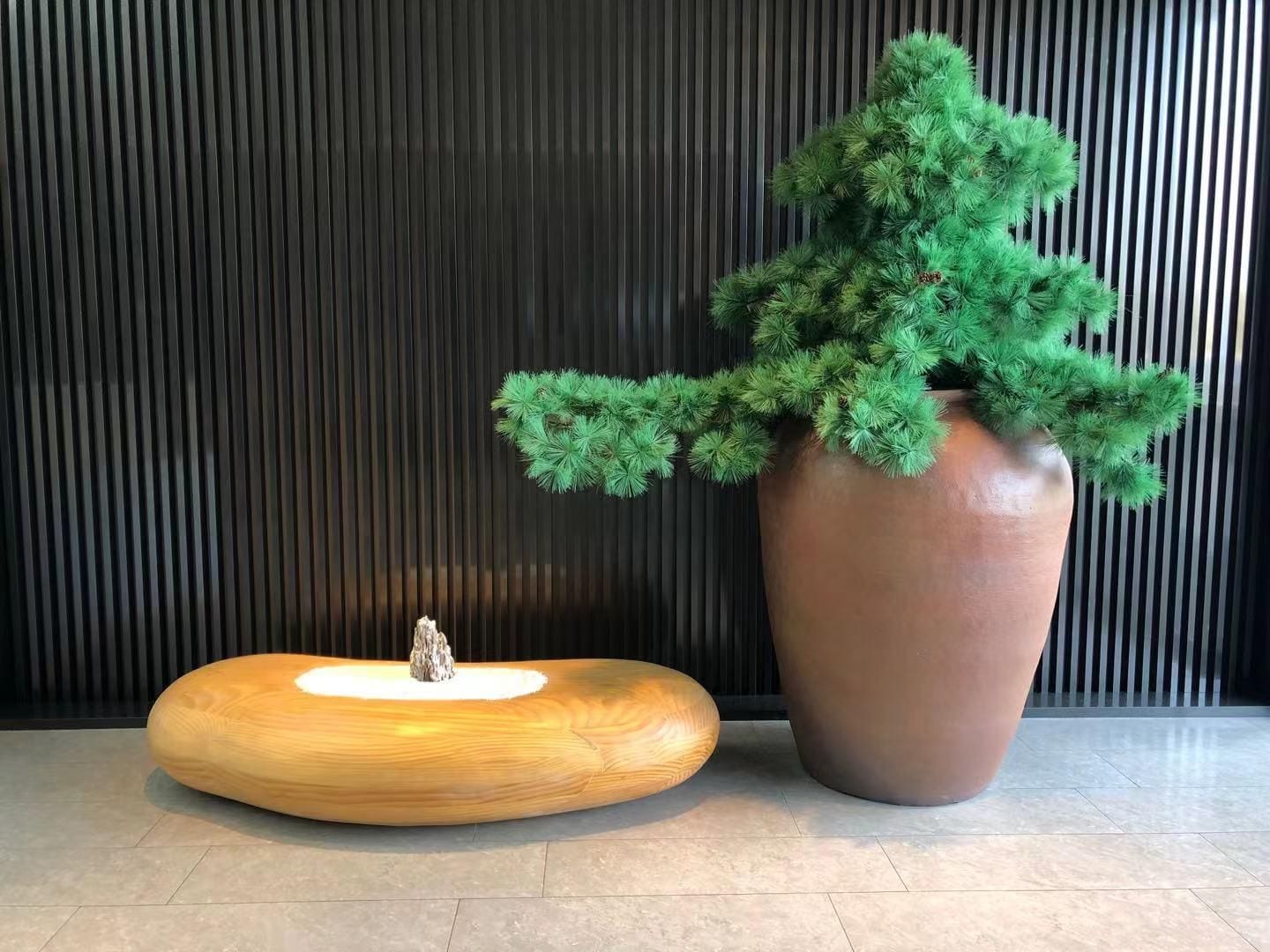 A wooden bench with a small tree stump centerpiece, a large potted plant, and a vertical striped wall.