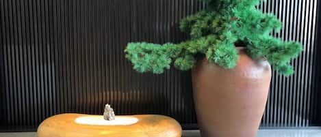 A wooden bench with a small tree stump centerpiece, a large potted plant, and a vertical striped wall.