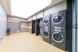 A modern laundry room with four stacked washing machines, a bench, and a small table.