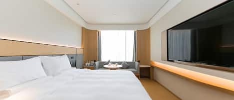 Habitación de hotel con una cama grande, televisión montada en la pared, una mesita con una silla y una ventana con cortinas.