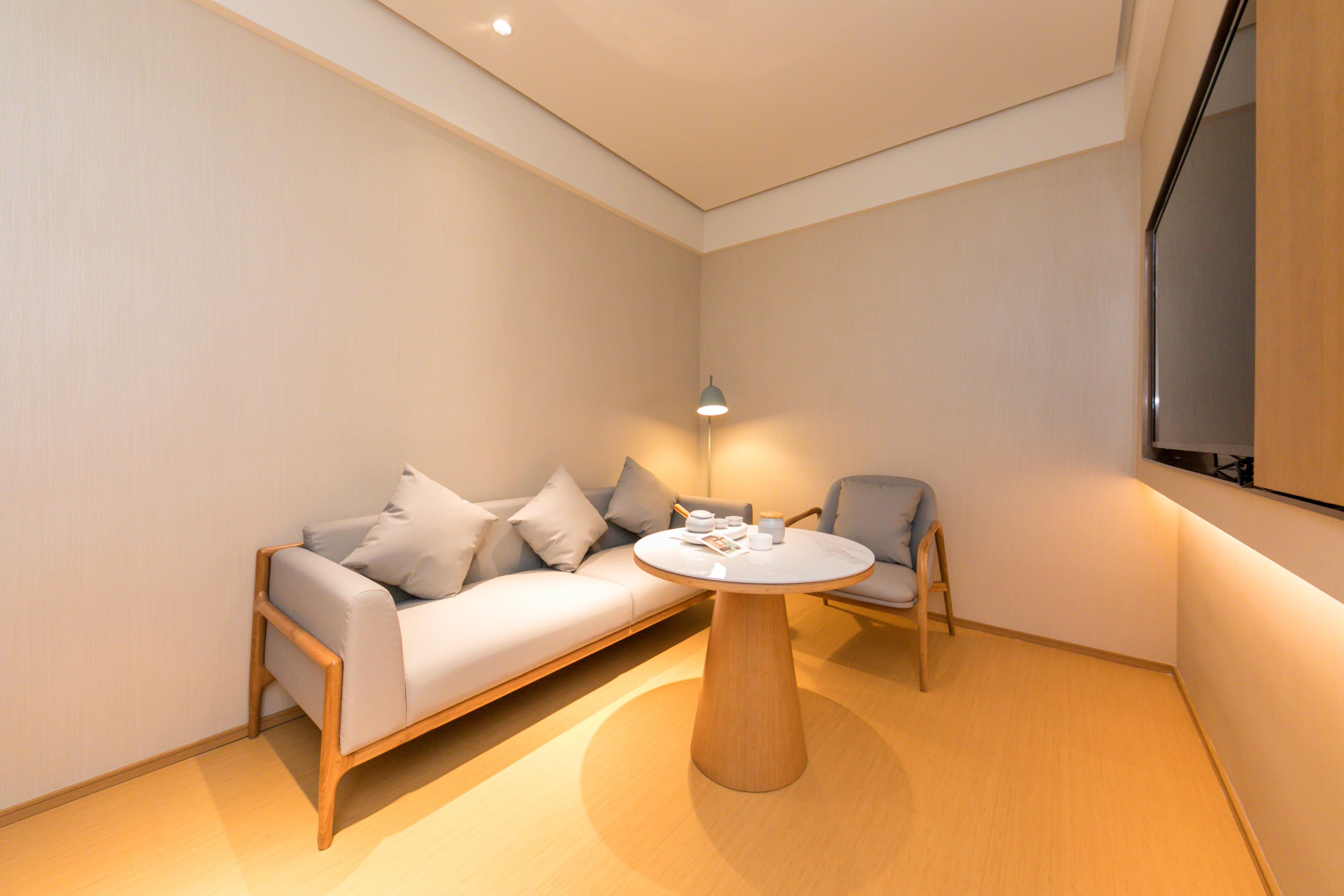 Una habitación moderna con sofá, una silla, una mesa redonda de madera y una lámpara.