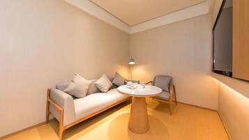 Una habitación moderna con sofá, una silla, una mesa redonda de madera y una lámpara.