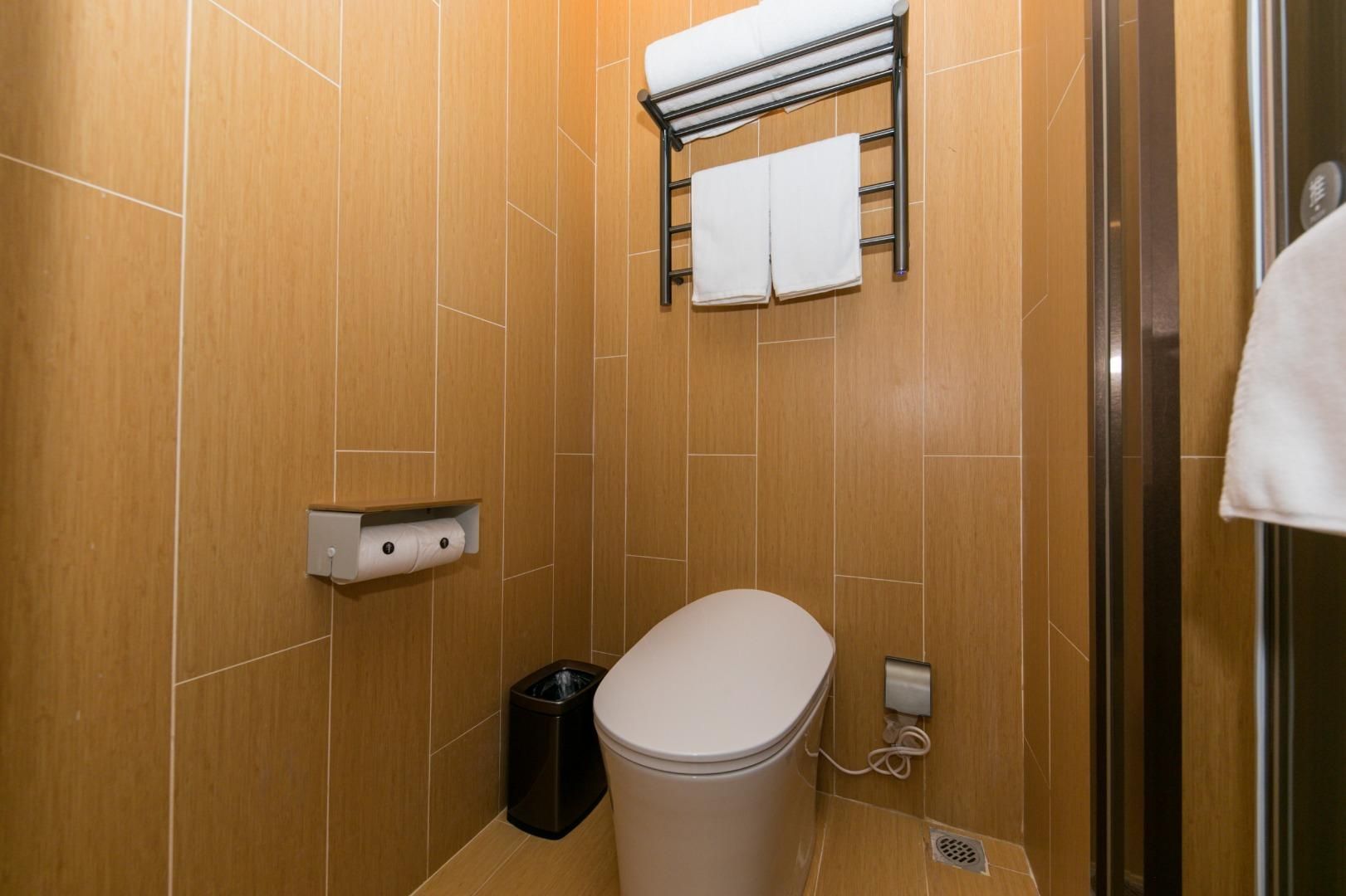 A small, modern bathroom with a toilet, a trash bin, a towel rack with two towels, and a paper towel dispenser.
