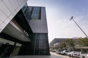 A modern building with a glass facade, a prominent entrance, and a parking area with cars. - Ji Hotel (hefei South Railway Station North Square (Hefei)