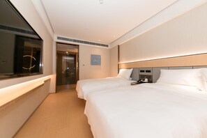 A hotel room with two beds, a bedside table with a phone and a cup, a window with blinds, and a door leading to a hallway.