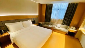 A hotel room with a large bed, a sofa, a small table with a tray, and a nightstand with a phone. - Ji Hotel (Nanjing)