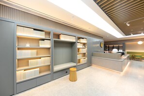 A modern library with bookshelves, a reception desk, and a wooden stool. - Ji Hotel (Nanjing)