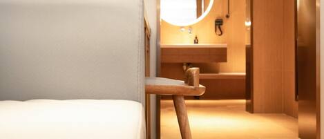 A modern hotel room with a wooden bed frame, a round mirror, and a wooden floor.