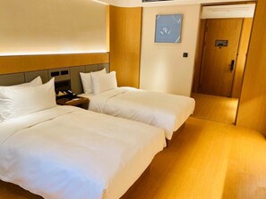 A hotel room with two beds, a bedside table with a phone, a wall-mounted artwork, and a wooden door. - Ji Hotel (Nanjing)