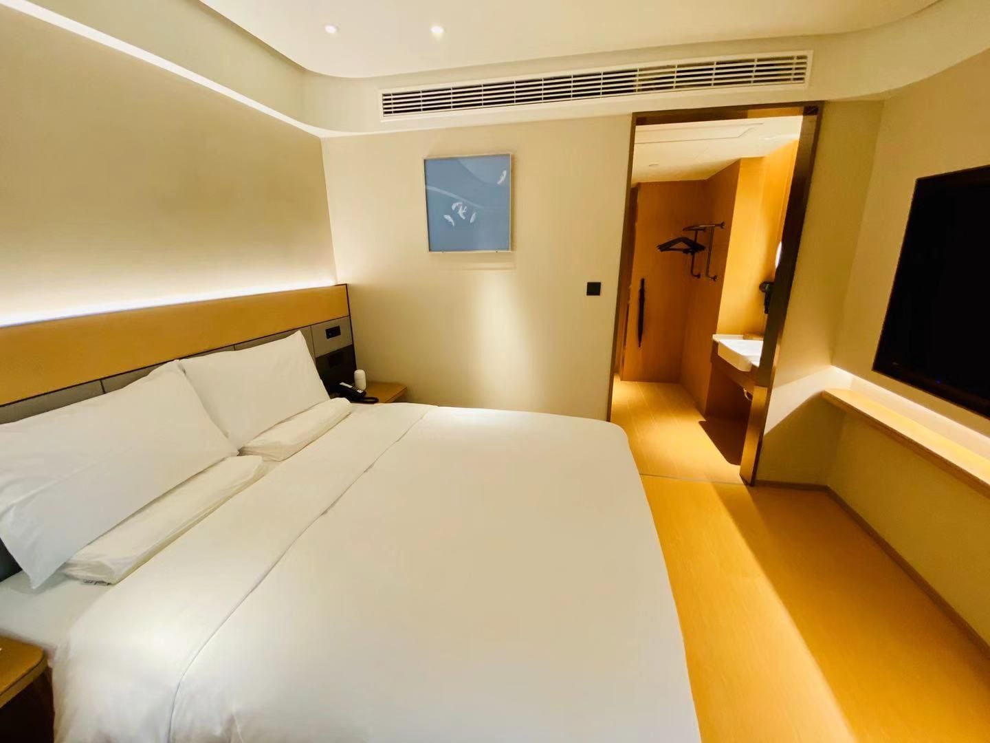 A hotel room with a large bed, a bedside table with a phone, a TV mounted on the wall, and a bathroom visible through an open door.