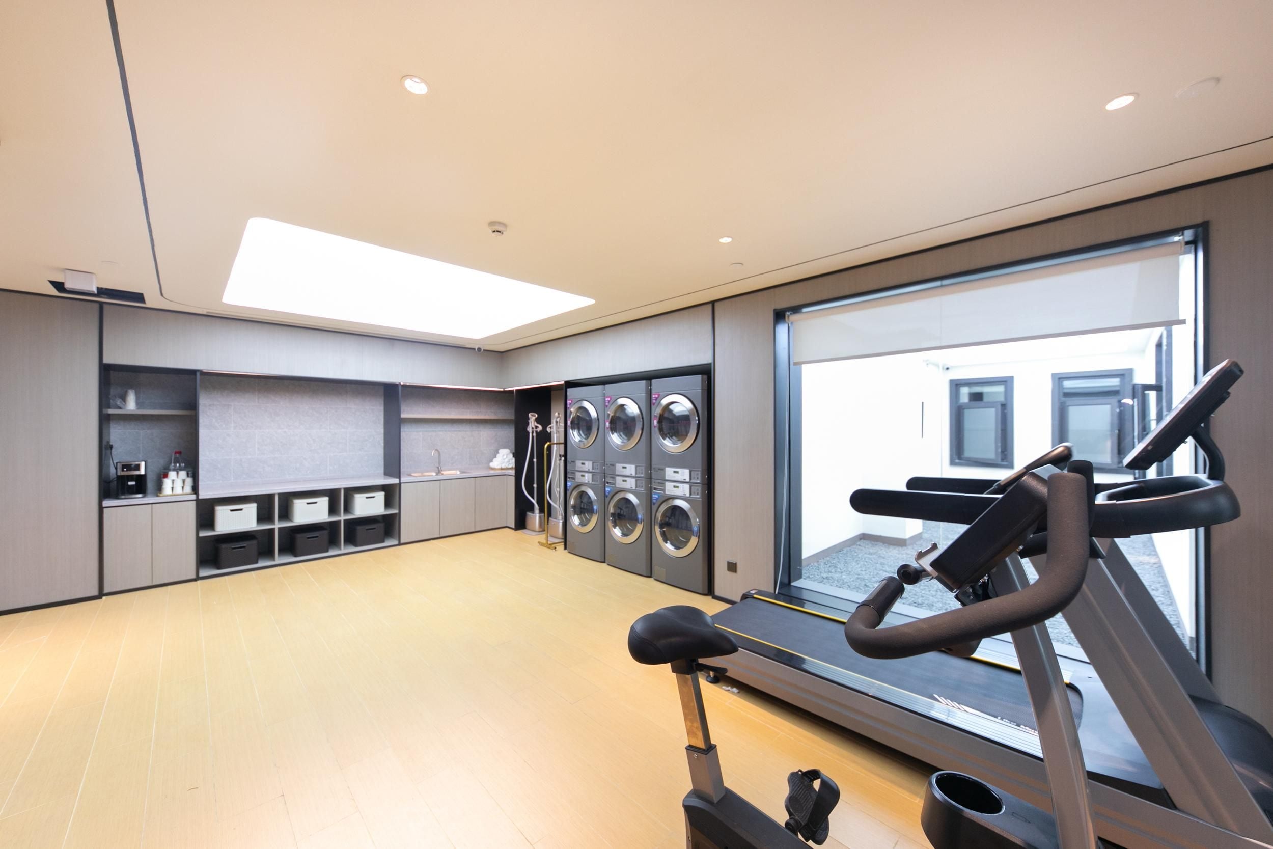 Ein Fitnessraum mit Laufband, Wandtrainingsgeräten und einem großen Fenster.