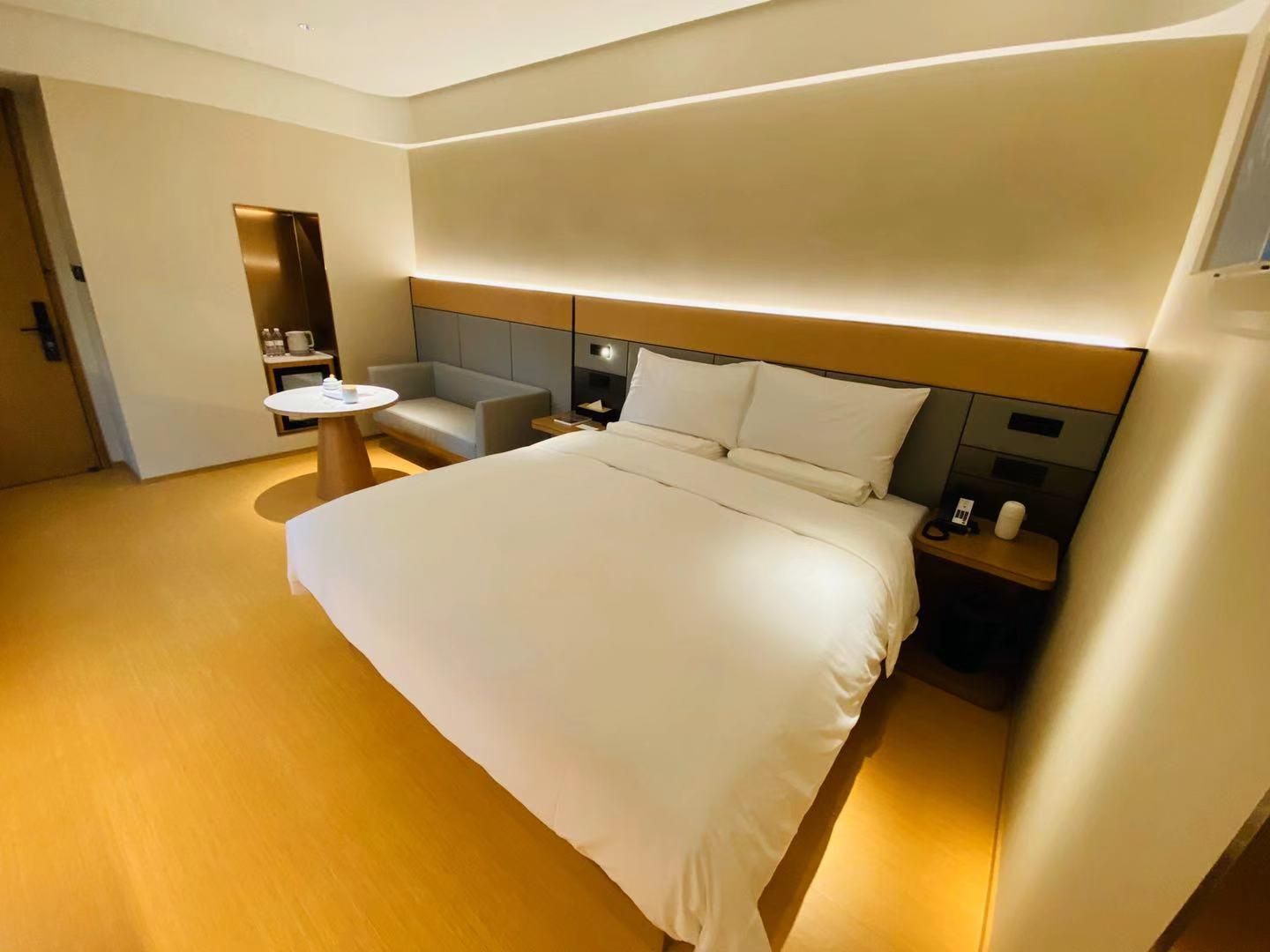 A hotel room with a large bed, a bedside table, a chair, a small round table, and a built-in shelf.
