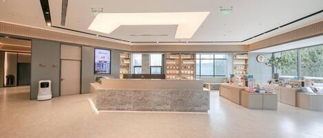 A modern hotel lobby with a reception desk, a large digital screen, and a view of the outdoors.