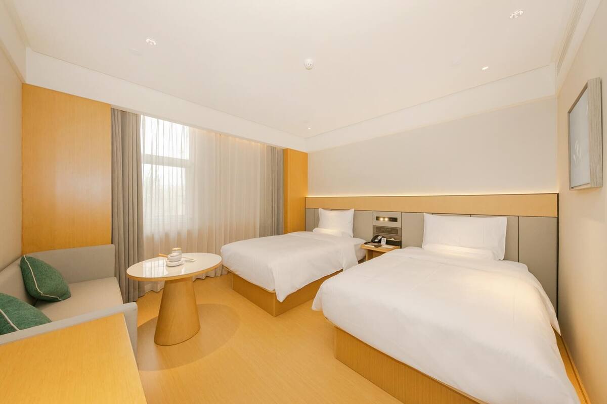 A hotel room with two beds, a round table, a sofa, and a nightstand with a phone.