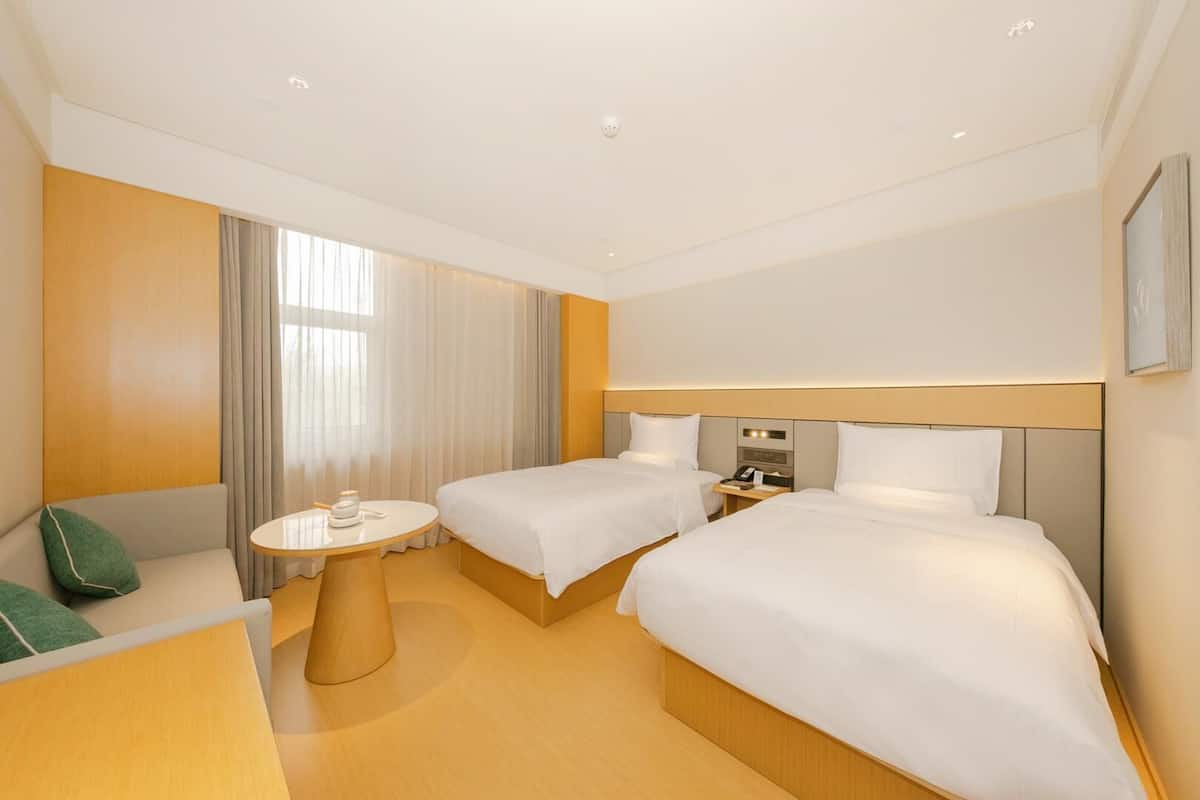 A hotel room with two beds, a round table, a sofa, and a nightstand with a phone.