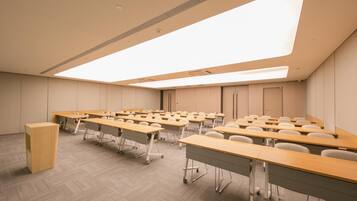 A conference room with rows of tables and chairs, a podium, and a skylight.