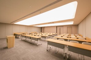 Un salón de conferencias con filas de mesas y sillas, un atril y un tragaluz.