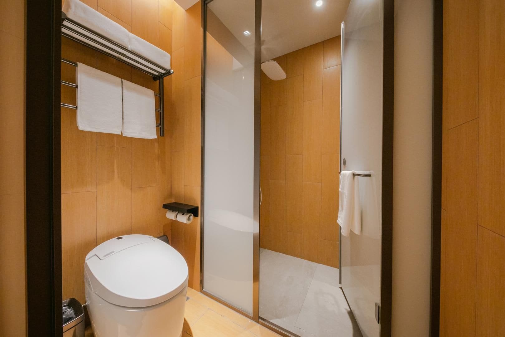 Un baño moderno con inodoro, cabina de ducha de vidrio y paredes de madera.