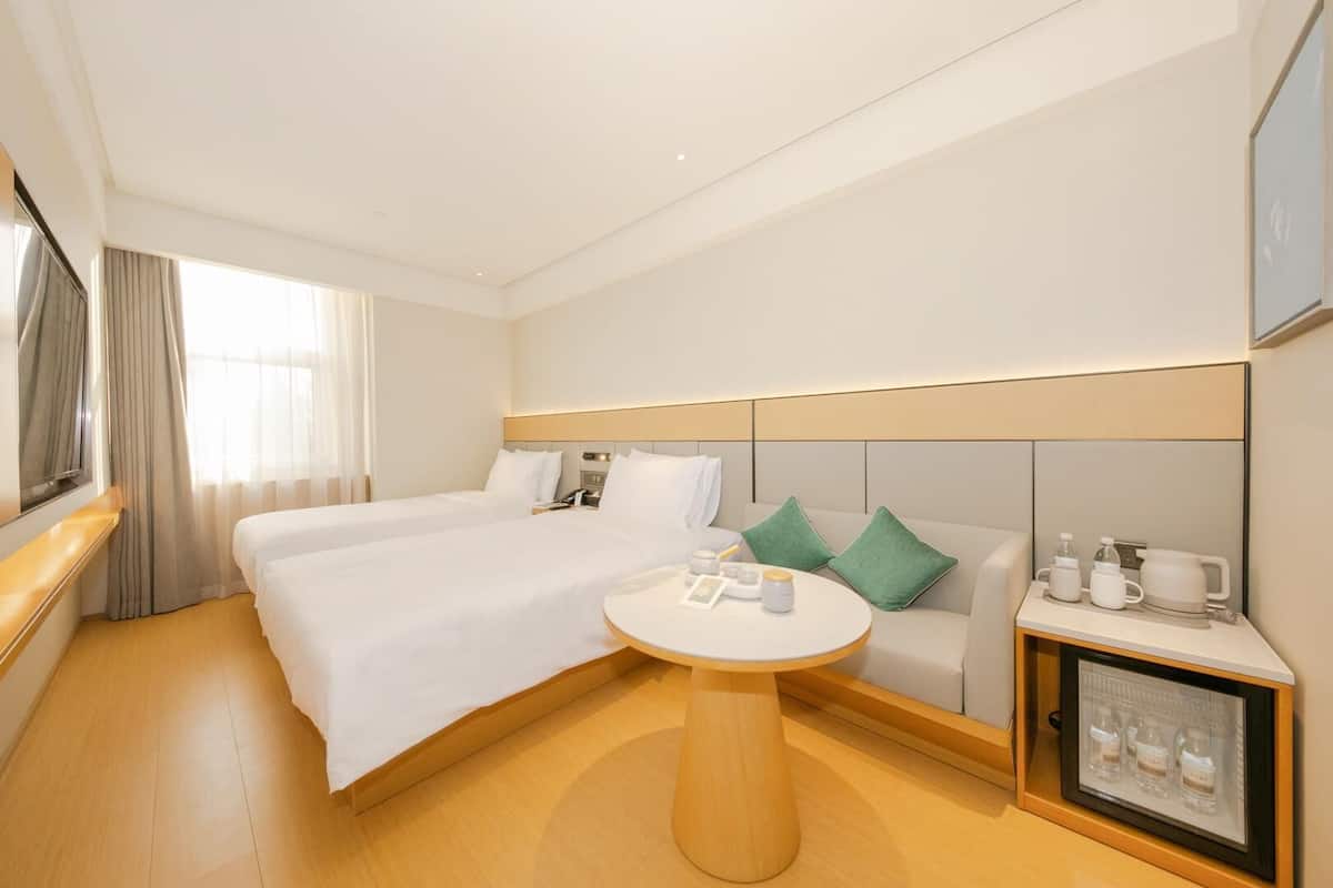 A hotel room with a large bed, a round table, a sofa, and a minibar.