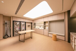 Une buanderie moderne équipée de machines à laver et de sèche-linge encastrés, d’une table et d’étagères de rangement.