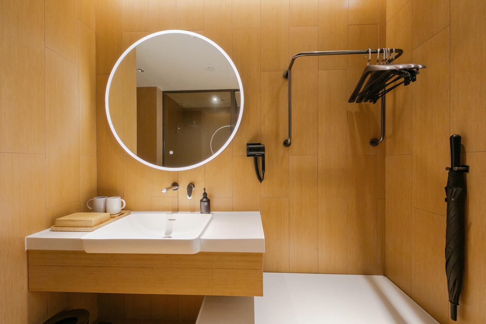 Un baño moderno con un espejo redondo, un lavamanos, un cabezal de ducha manual y un perchero para toallas.