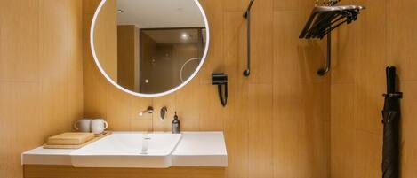 Un baño moderno con un espejo redondo, un lavamanos, un cabezal de ducha manual y un perchero para toallas.