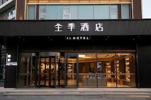 Entrada de hotel con diseño moderno, puertas de vidrio y un interior visible con asientos y decoración.
