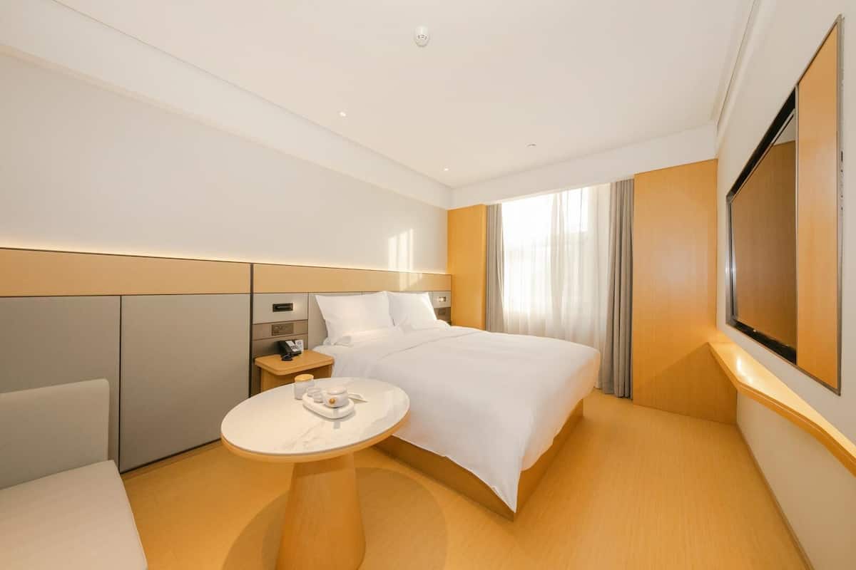 A hotel room with a bed, bedside table, and a small round table with a tray.
