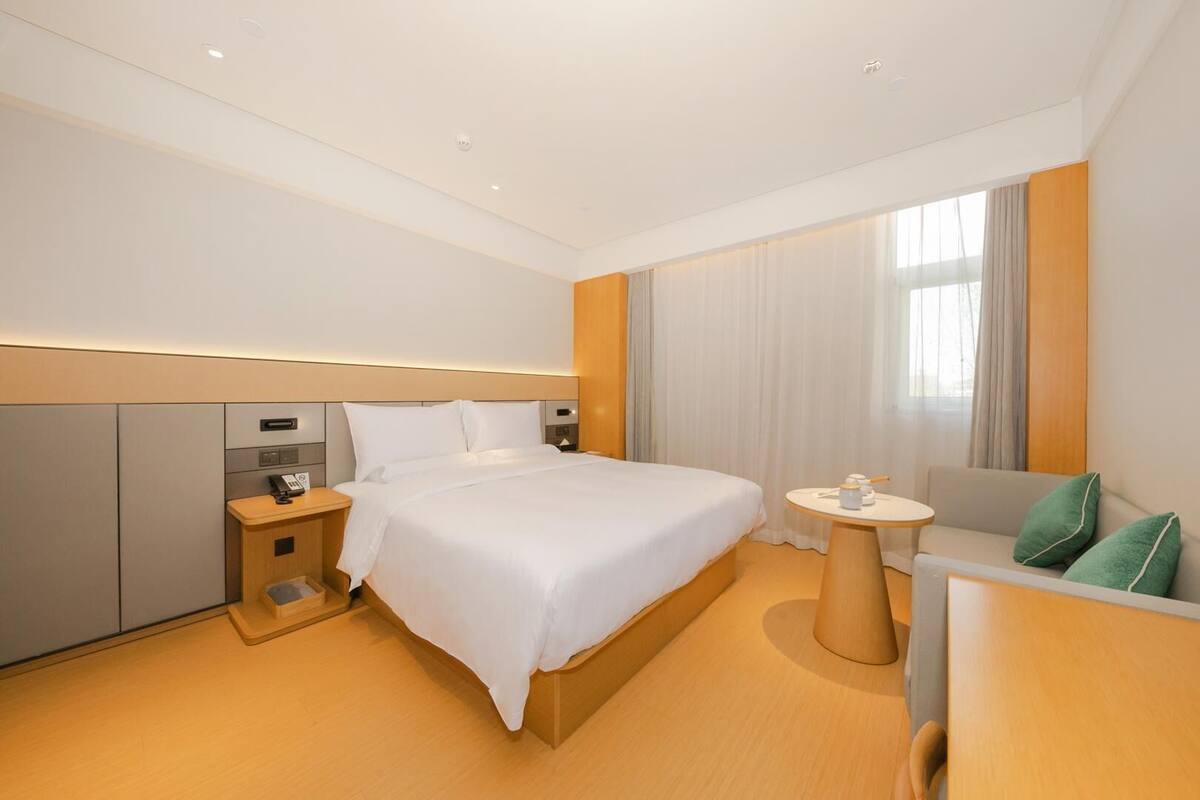 A modern hotel room with a large bed, bedside tables, a small sofa, and a desk with a chair.