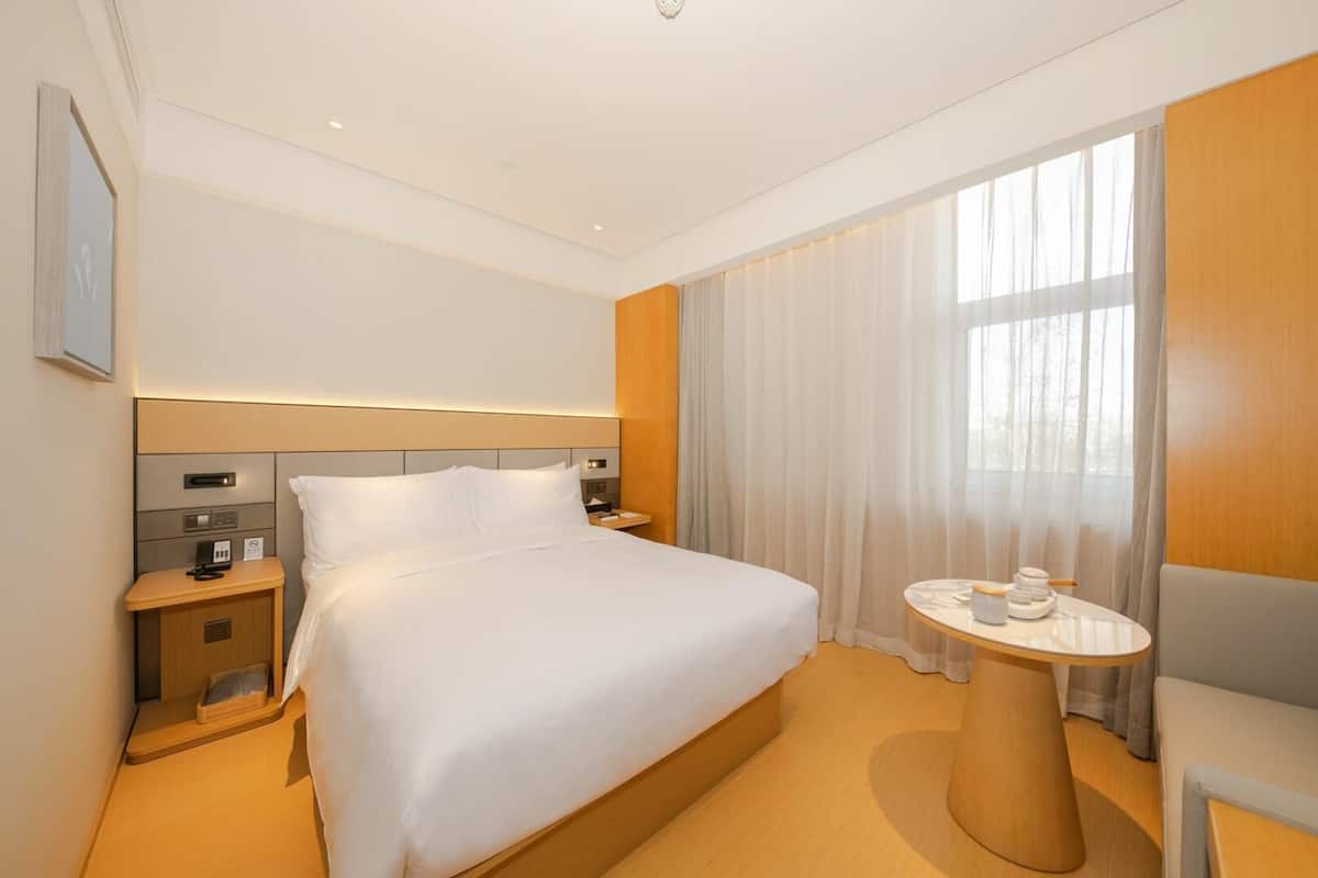 A hotel room with a large bed, bedside tables, a small round table, and a window with curtains.