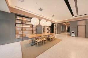Eine großzügige, moderne Bibliothek mit einem langen Holztisch und Stühlen, umgeben von Bücherregalen und Pendelleuchten.