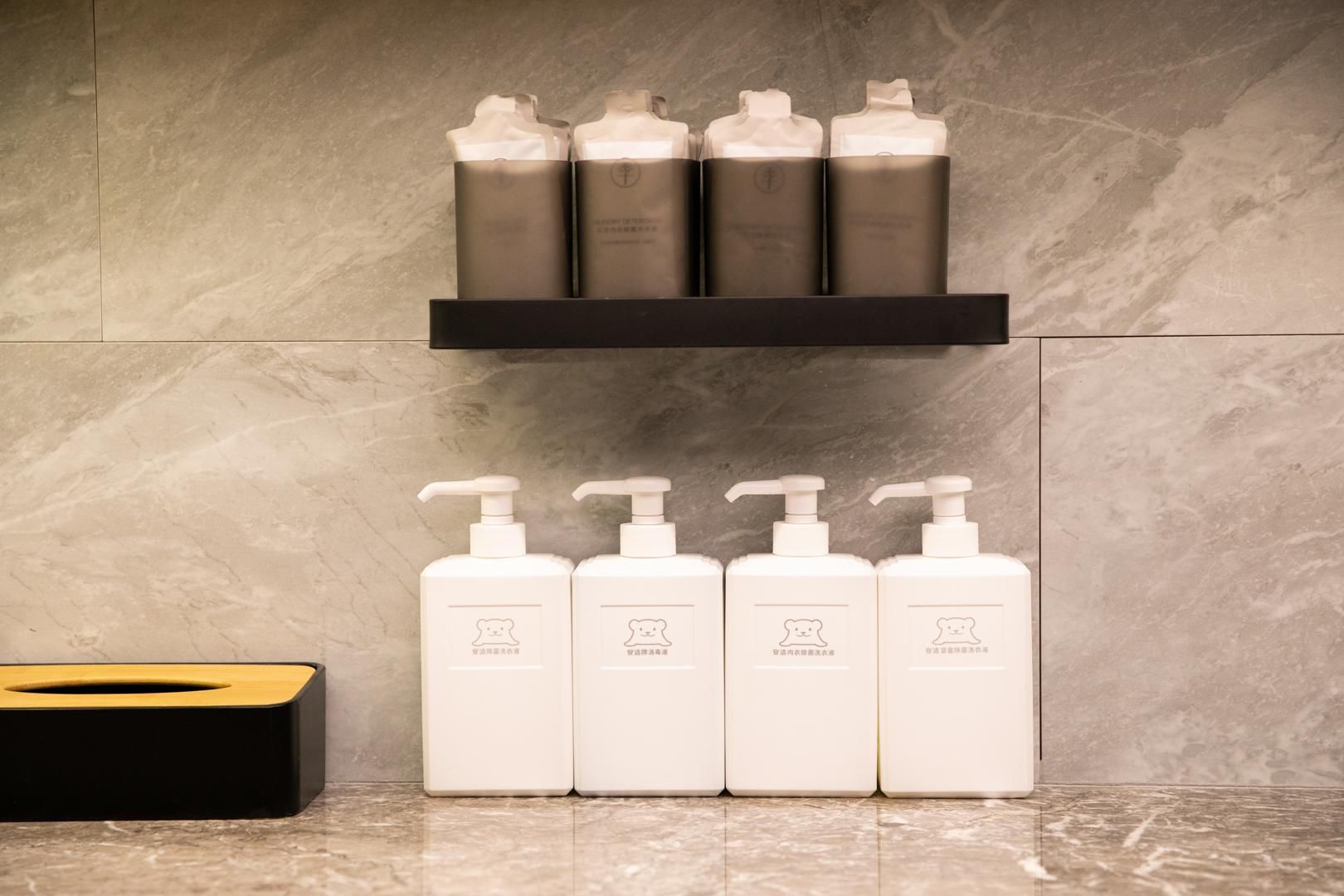 A bathroom with a marble wall, a black shelf holding four bottles, and a black tissue box.