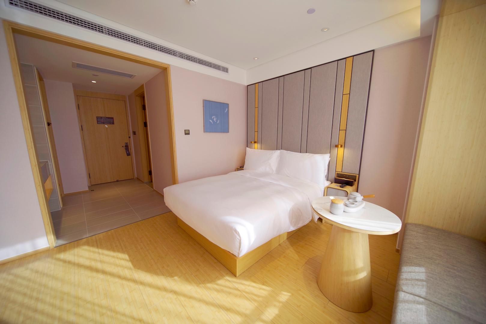 A hotel room with a large bed, a bedside table, a small round table, and a door leading to another room.