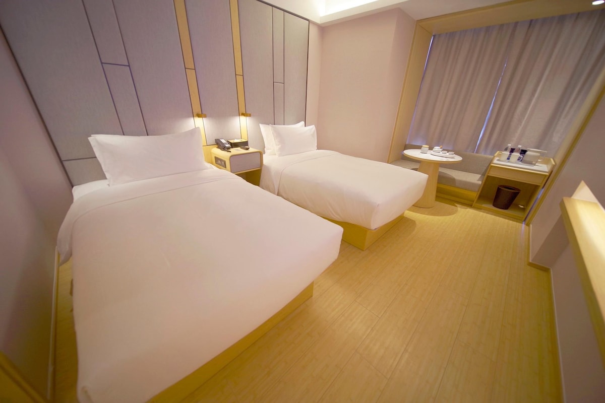 Habitación de hotel con dos camas, una mesita redonda pequeña, una mesita de noche con teléfono y una ventana con cortinas.