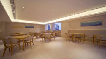 A spacious room with multiple tables and chairs, a high ceiling with recessed lighting, and artwork on the walls.