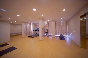 Una habitación amplia con cinta de correr, elíptica y tapete de yoga.