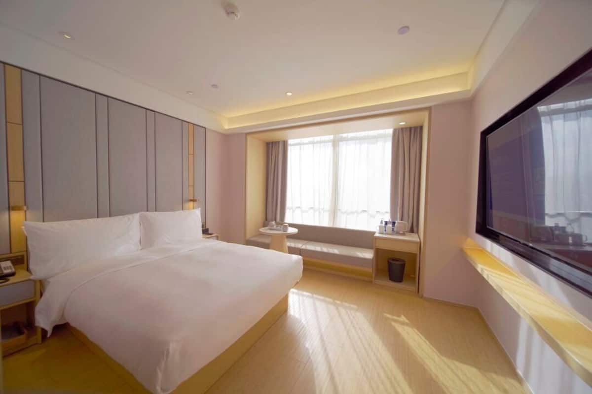 Una habitación de hotel con una cama grande, televisión, ventana con cortinas y una pequeña mesa.