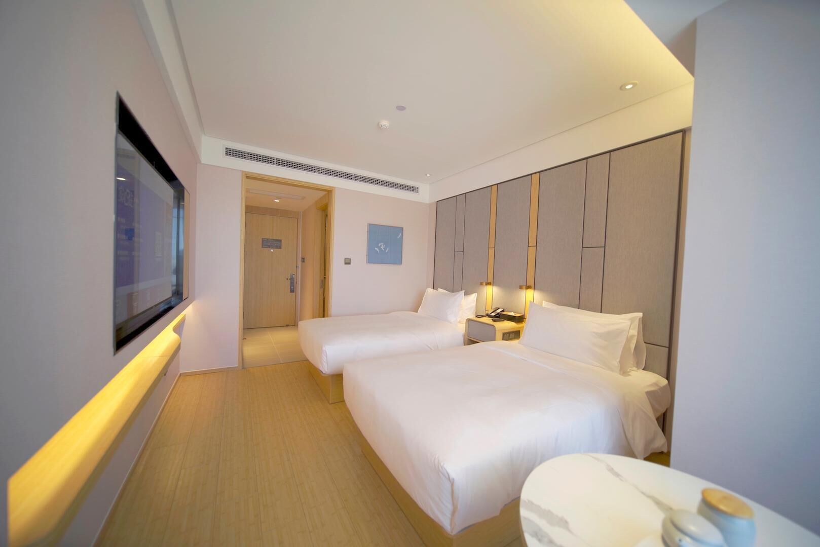 Ein Hotelzimmer mit zwei Betten, einem Fernseher, einem Nachttisch und einer Tür zu einem weiteren Raum.
