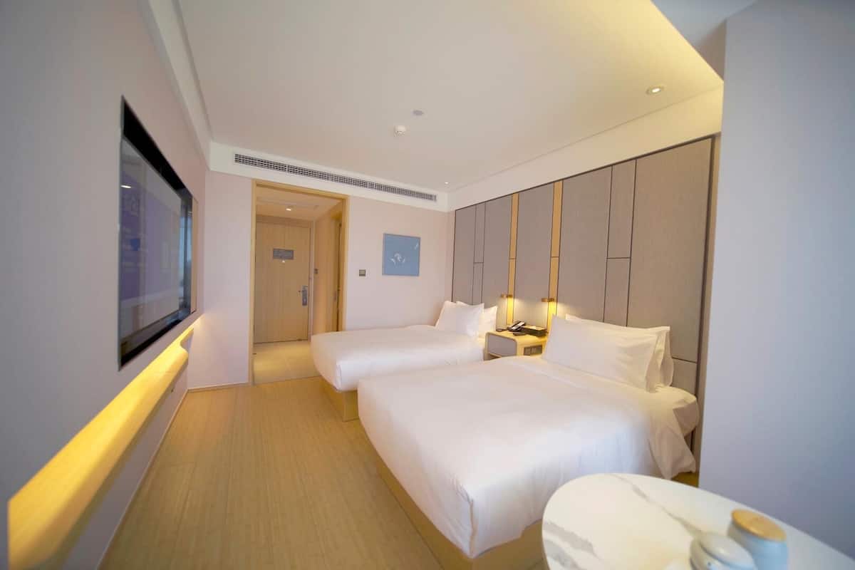 Habitación de hotel con dos camas, un televisor, una mesita de noche y una puerta que da a otra habitación.