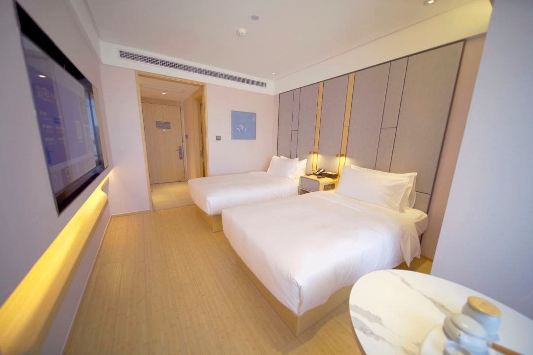 A hotel room with two beds, a TV, a bedside table, and a wooden floor.