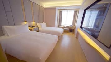 Quarto de hotel com duas camas, uma mesa pequena, televisão e janela com cortinas.