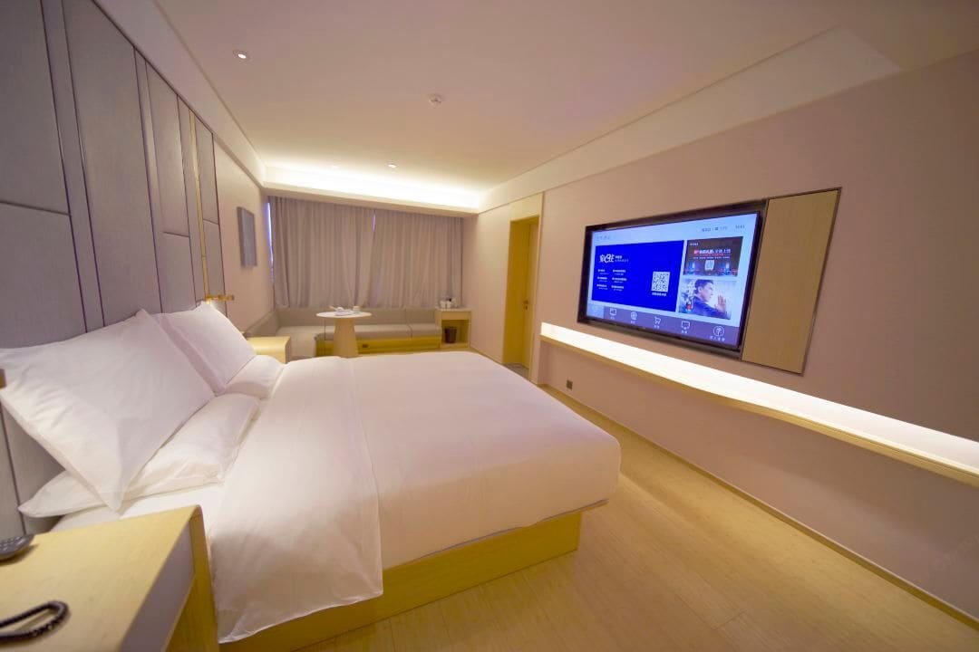A modern hotel room with a large bed, a TV mounted on the wall, and a bedside table.