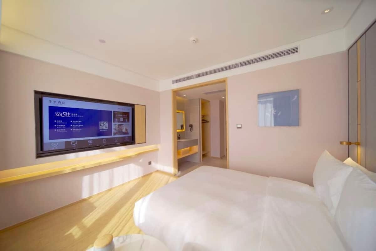 Habitación de hotel con cama, televisor montado en la pared, baño con lavabo y puerta que da a otra habitación.