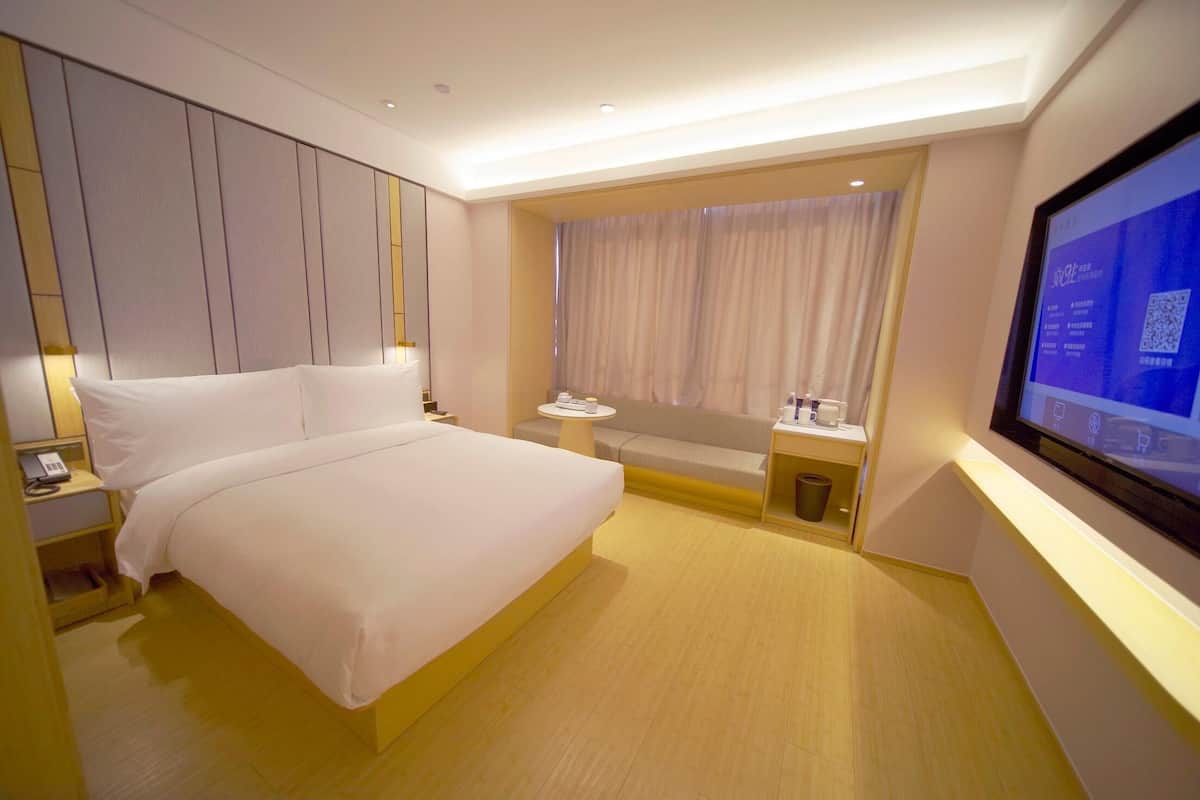 Habitación de hotel con una cama grande, mesita de noche con teléfono, una pequeña mesa redonda con una taza y plato, un sofá y un televisor montado en la pared.